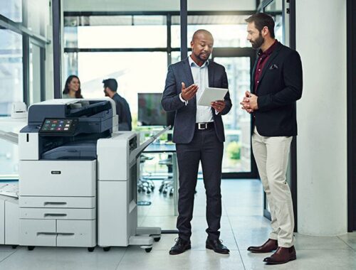 Twee mannen in een kantooromgeving die iets bespreken op een tablet naast een Xerox® AltaLink® C8200 Series Colour Multifunction Printer